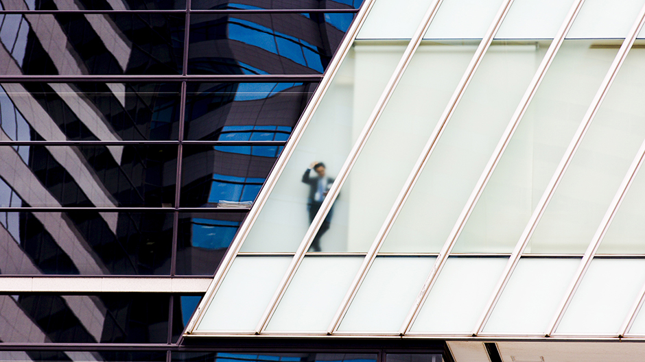 A businessman stands behind a frosted glass window of an office high-rise in central Tokyo June 9, 2015.