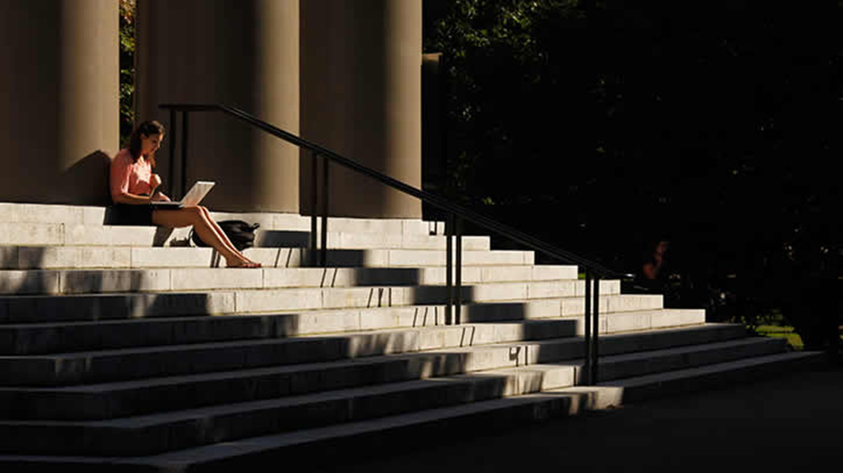 A student uses her laptop computer on the steps to Memorial Church at Harvard University in Cambridge, Massachusetts